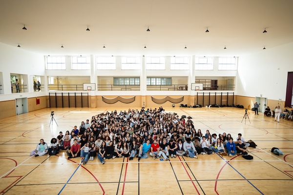 Os alunos da escola sentados no chão do pavilhão, em torno do espaço da gravação.