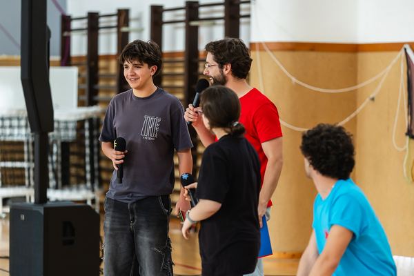 Os apresentadores conversam com uma aluna, de microfone na mão, antes do início da gravação.
