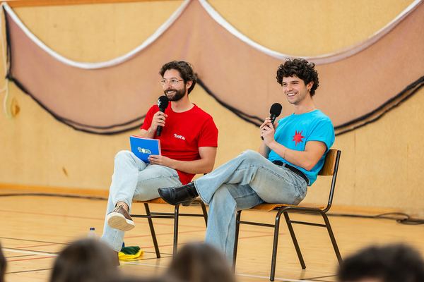 Os dois apresentadores do BORA, sentados com microfones, durante a gravação do episódio.