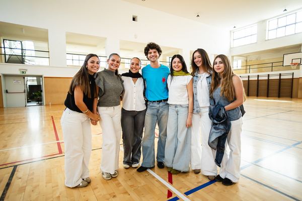 Grupo de alunas e alunos posa com os apresentadores no pavilhão.