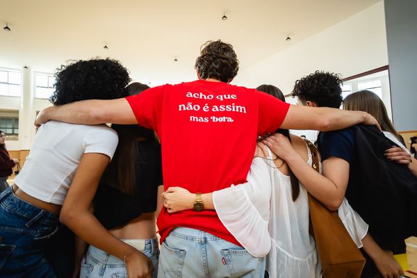 Alunos e apresentadores abraçados, de costas, no meio do pavilhão.
