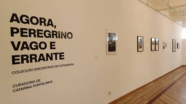 Parede da Sala de Exposições com o título «Agora, peregrino vago e errante», «Colecção Encontros de Fotografia, curadoria de Catarina Portelinha», e fotografias emolduradas ao longo da parede.
