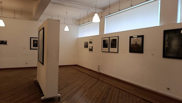 Vista da sala com um painel em primeiro plano e, na parede do fundo, uma sequência de fotografias emolduradas a preto e branco.