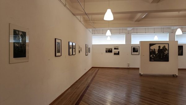 Vista da sala com fotografias emolduradas na parede e, ao fundo, um painel com uma fotografia de grande formato de um grupo de pessoas.