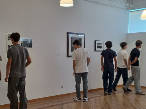Alunos a percorrer a exposição junto às fotografias emolduradas, durante uma visita à sala.