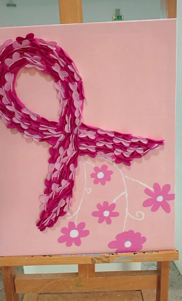 Tela cor-de-rosa num cavalete com um grande laço feito de pequenos corações de feltro em vários tons de rosa e flores pintadas por baixo.